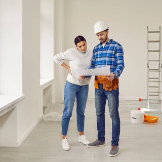 Jeune femme en plan de rénovation d'une maison avec un homme portant un casque