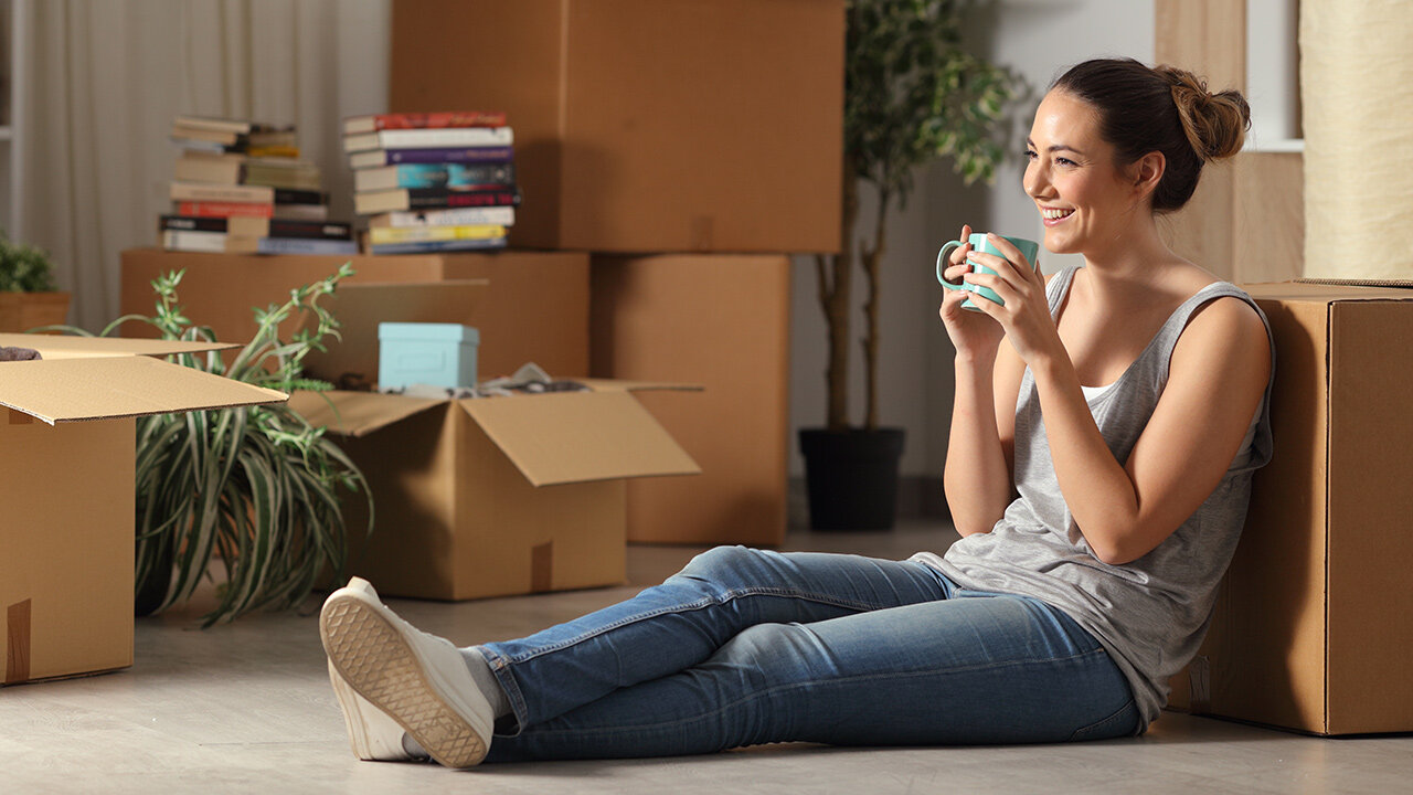 Jeune femme souriante buvant une boisson, assise adossée à un carton