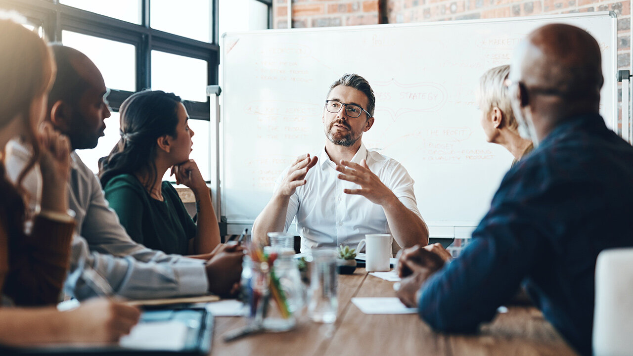 Groupe de personnes en réunion autour d'une table devant un tableau blanc